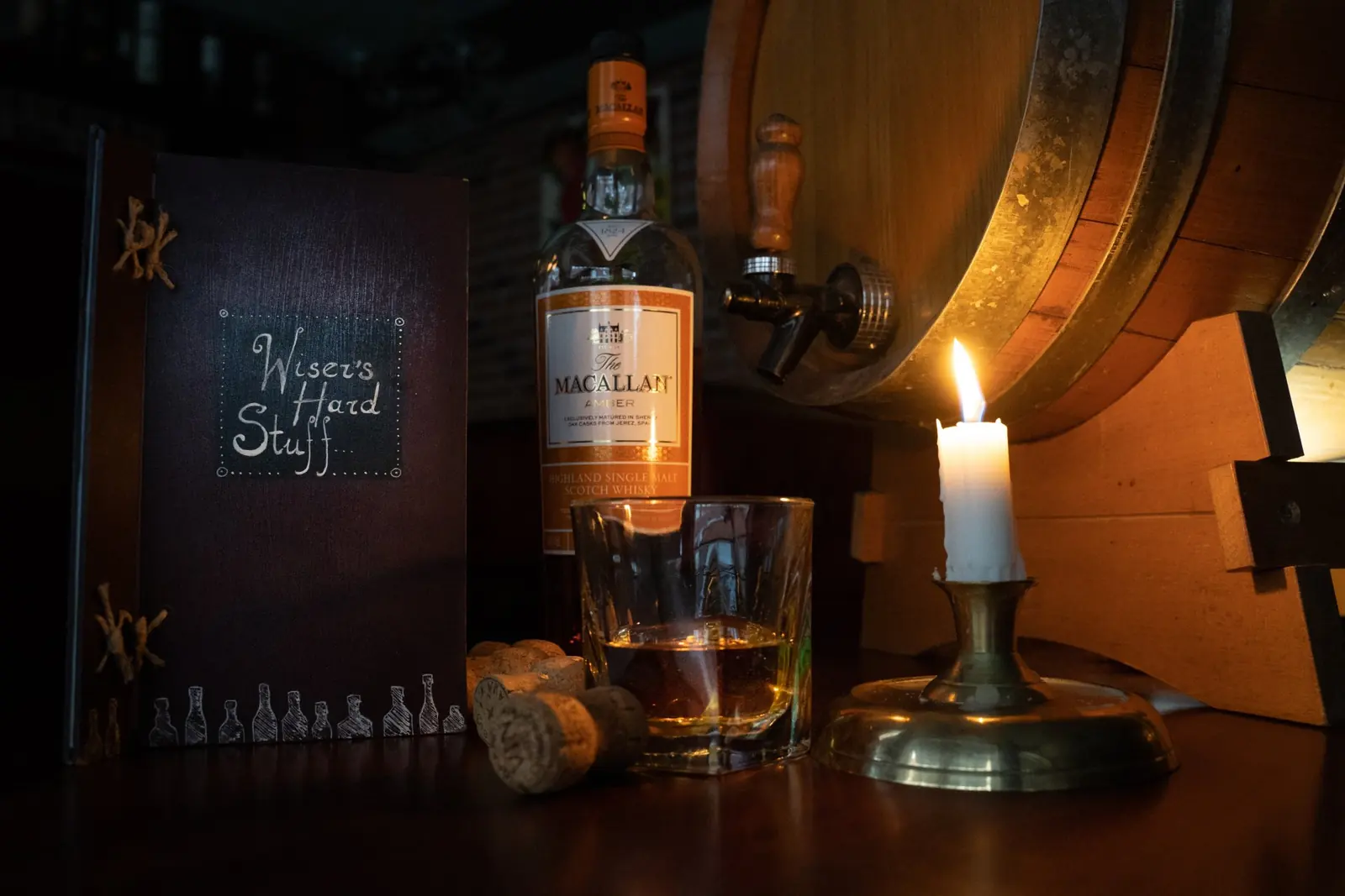 Ett glas whisky bredvid ett levande ljus och en tunna